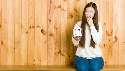 Young asian woman holding a house icon relaxed thinking about something looking at a copy space.