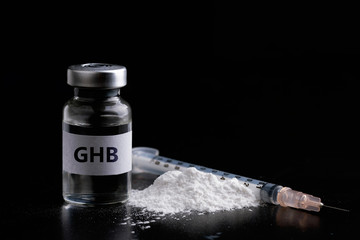 Bottle of GHB with a syringe in black background.Dangerous drug women