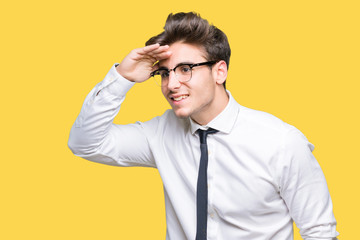 Young business man wearing glasses over isolated background very happy and smiling looking far away with hand over head. Searching concept.