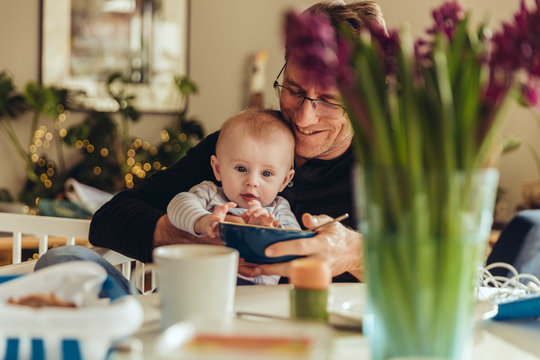 Baby auf Papas Scho&szlig; greift nach einer Schale mit Essen