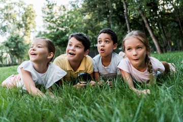selective focus of surprised multicultural children  lying on grass