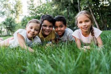 Fototapeta premium selective focus of cute multicultural children smiling while lying on grass