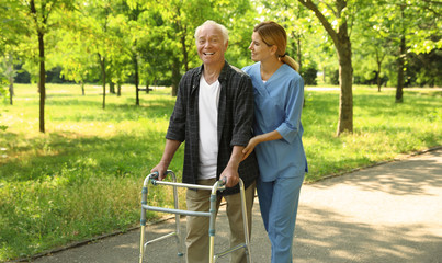 Happy nurse assisting elderly man with walking frame at park