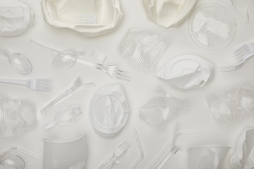 top view of crumpled disposable cups, forks, spoons and plates on white background