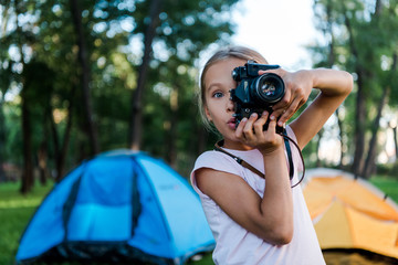 surprised kid holding digital camera while taking photo near camps