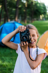 happy kid holding digital camera while taking photo near camps