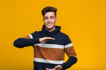Young cool man wearing a hoodie holding something with both hands, product presentation. - Powered by Adobe