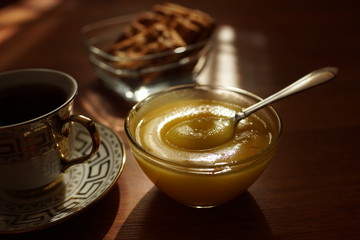 Tea time. Honey in a glass bowl with a spoon, a cup of tea on a saucer, cookies in a vase on the table.