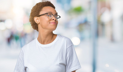 Beautiful young african american woman wearing glasses over isolated background looking away to side with smile on face, natural expression. Laughing confident.