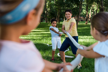 selective focus of happy multicultural kids competing in tug of war outside