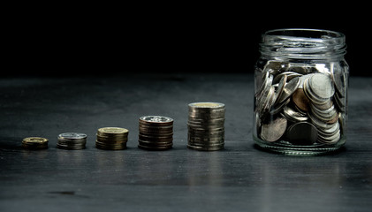 growth graph from stack of coin and clear jar with thai baht coin on black background. concept for financial and saving money