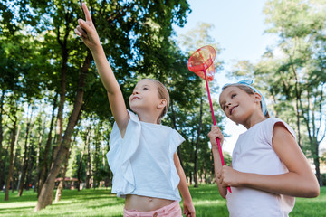 cute kid pointing with finger near happy friend with butterfly net