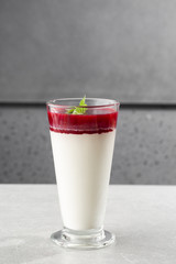Delicious italian dessert panna cotta with berry sauce and mint on gray background. Traditional italian dessert. Vertical photo.