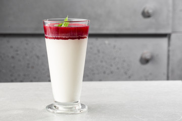 Delicious italian dessert panna cotta with berry sauce and mint on gray background. Traditional italian dessert. Horizontal photo.