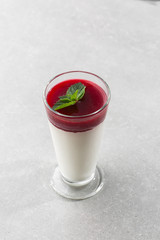 Delicious italian dessert panna cotta with berry sauce and mint on gray background. Traditional italian dessert. Vertical photo.