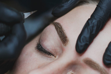 master in black gloves makes permanent eyebrow makeup close-up 1
