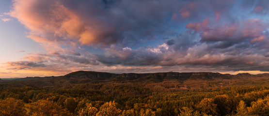 Autumn landscape at sunset - mountains, forests and beautiful clouds illuminated by the setting sun, hills of Bohemian Switzerland and Saxon Switzerland National Park, Czech Republic and Germany