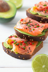 Sandwich with salmon, avocado, sesame, lime and chili pepper on a white wooden background.