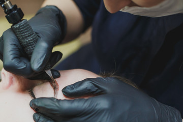 master in black gloves makes permanent eyebrow makeup close-up 1