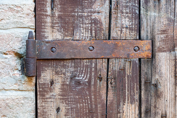 Window detail of rural house, with cracked paint and rusty hinges, on brick wall and ancient stones.