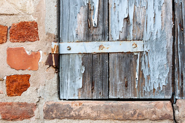 Window detail of rural house, with cracked paint and rusty hinges, on brick wall and ancient stones.