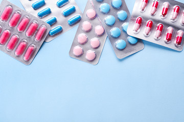 Flat lay composition with bunch of different colorful pills in blister packs. Pile of unpacked medication on paper textured background. Close up, copy space.