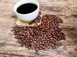 A cup of black cofee and Coffee beans are on the wooden table, ready to give freshness and alongside the businessman