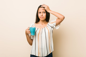 Young hispanic woman holding a cup being shocked, she has remembered important meeting.