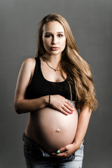 Beautiful pregnant woman in bodysuit with makeup on a dark background. Fashion photo stylish portrait of a young girl