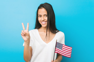 Young hispanic woman holding a united states flag showing number two with fingers.