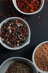 Paprika, mustard, caraway seeds and a mixture of peppercorns in white ceramic bowls next to the mortar isolated on black background