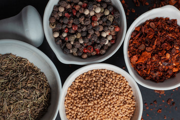 Paprika, mustard, caraway seeds and a mixture of peppercorns in white ceramic bowls next to the mortar isolated on black background
