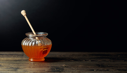 Honey in jar on a old wooden table, black background.