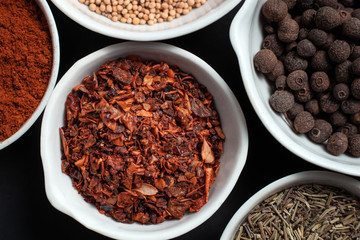 Paprika, mustard, caraway seeds and a mixture of peppers in white ceramic bowls next to the mortar isolated on black background