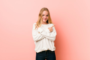 Young blonde teenager woman points sideways, is trying to choose between two options.