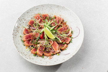 Close up of rare seared tuna slices with lime and arugula leaves on a plate. Gray background. Tuna salad. Top view from above horizontal.
