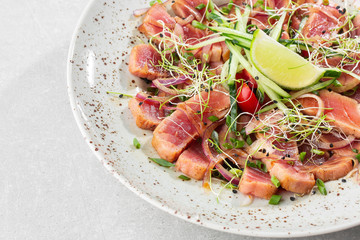 Close up of rare seared tuna slices with lime and arugula leaves on a plate. Gray background. Tuna salad. Top view from above horizontal.