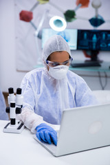 Focused female scientist wearing protection equipment working on her laptop