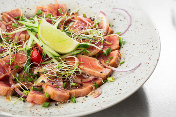 Close up of rare seared tuna slices with lime and arugula leaves on a plate. Gray background. Tuna salad. Top view from above horizontal.