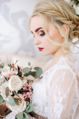 Obraz premium The bride holds in hands a beautiful wedding bouquet. Portrait of an elegant bride with professional makeup and hairstyle in a luxurious wedding dress. Wedding details and accessories, rustic wedding