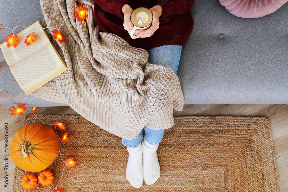 Wall mural Top view of woman relaxing on couch at home, drinking latte. Cozy evening at home. Young woman enjoying alone time, sitting on sofa covered with soft blanket. Close up, copy space.