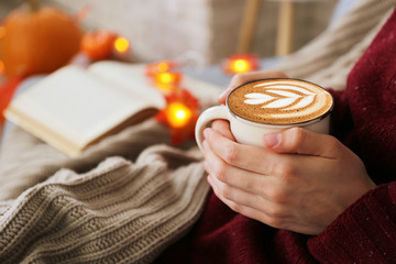 Top view of woman relaxing on couch at home, drinking latte. Cozy evening at home. Young woman...