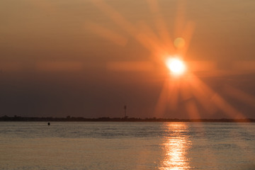Beautiful orange sunset over bay water area with streaking light flare effect casting rays through atmosphere