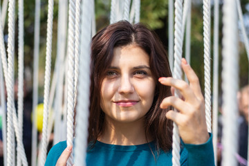 Smiling girl in aqua blue sweater standing among white ropes hanging down vertically like strings. Young woman posing. Closeup female portrait concept.