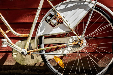 A classic white and rusty bike leaning against a wooden wall.