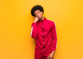 Young sport black man over an orange wall thinking of something, looking to the side