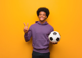 Young african american sport man holding a soccer ball showing number two