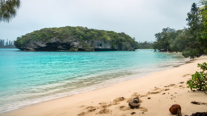 Kanumera Bay view at the beach with a small rocky island covered in vegetation at Isle of Pines, New Caledonia, South Pacific Ocean.