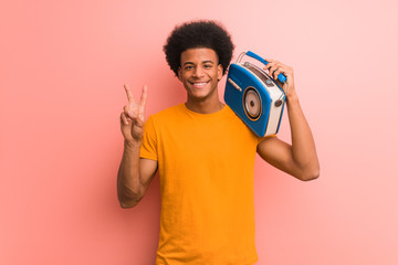 Young african american holding a vintage radio fun and happy doing a gesture of victory