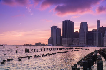 Obraz premium Beautiful view of downtown Manhattan skyline financial district as sun goes down in majestic sunset behind city cast purple color across evening sky